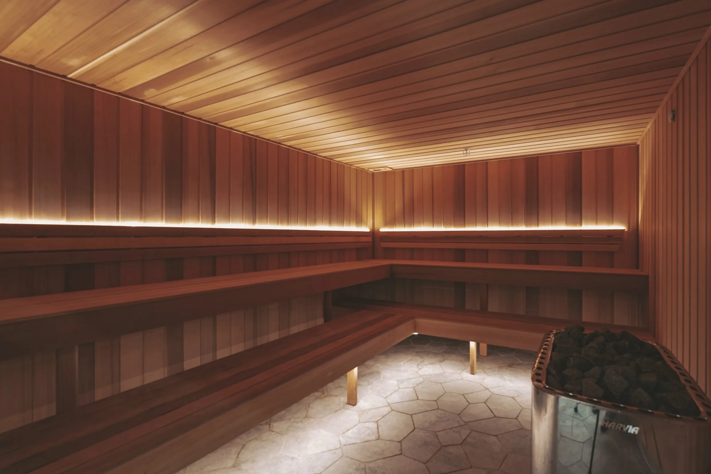 The cedar sauna: tiered benches under soft cove lighting, heater stones in the corner and a stone floor.
